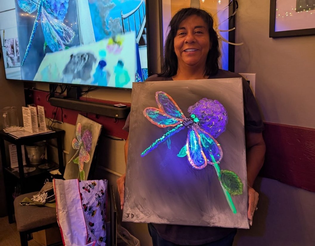 Guest holding a glowing dragonfly painting